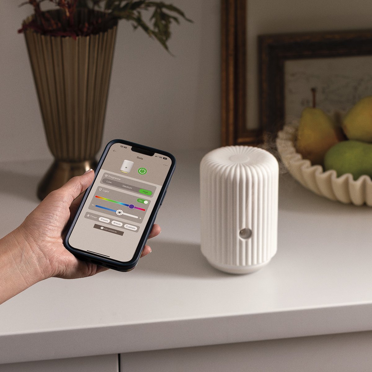 Scentsy Solo diffuser on a styled shelf while a hand adjusts it from the Scentsy app on a phone
